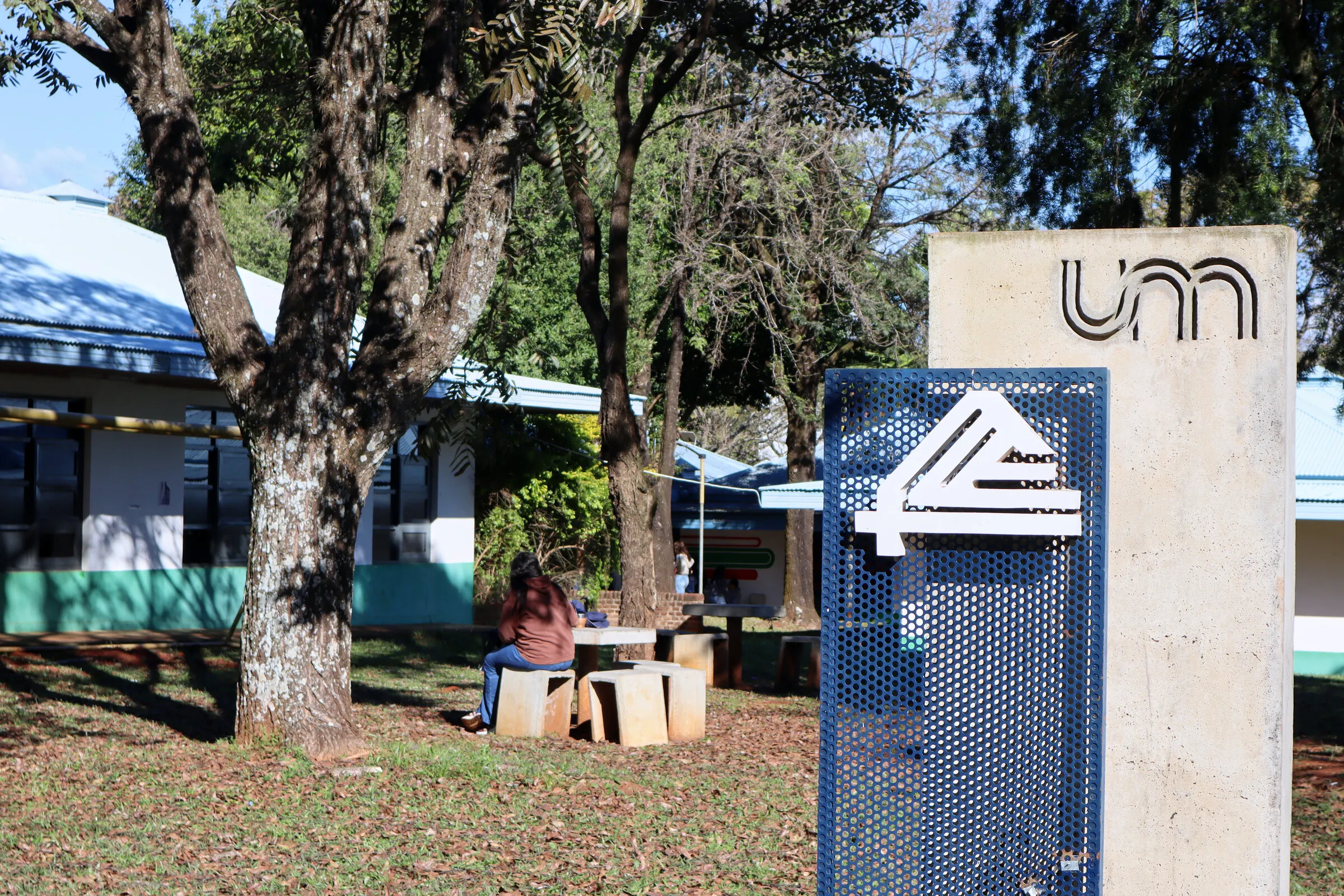 Predio de la Facultad de Ciencias Económicas de la UNaM, con el cartel de la Facultad y el monolito de la Universidad entre los árboles